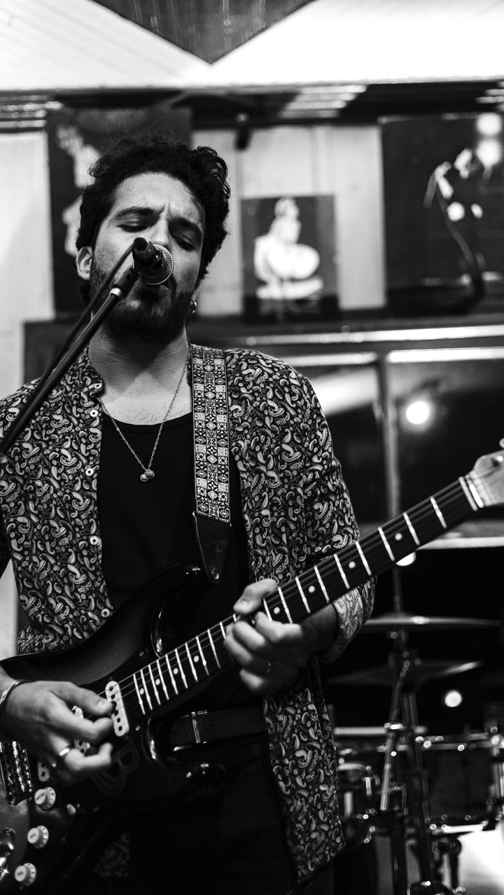 Bruno Bonafini cantando ao microfone com guitarra, em preto e branco